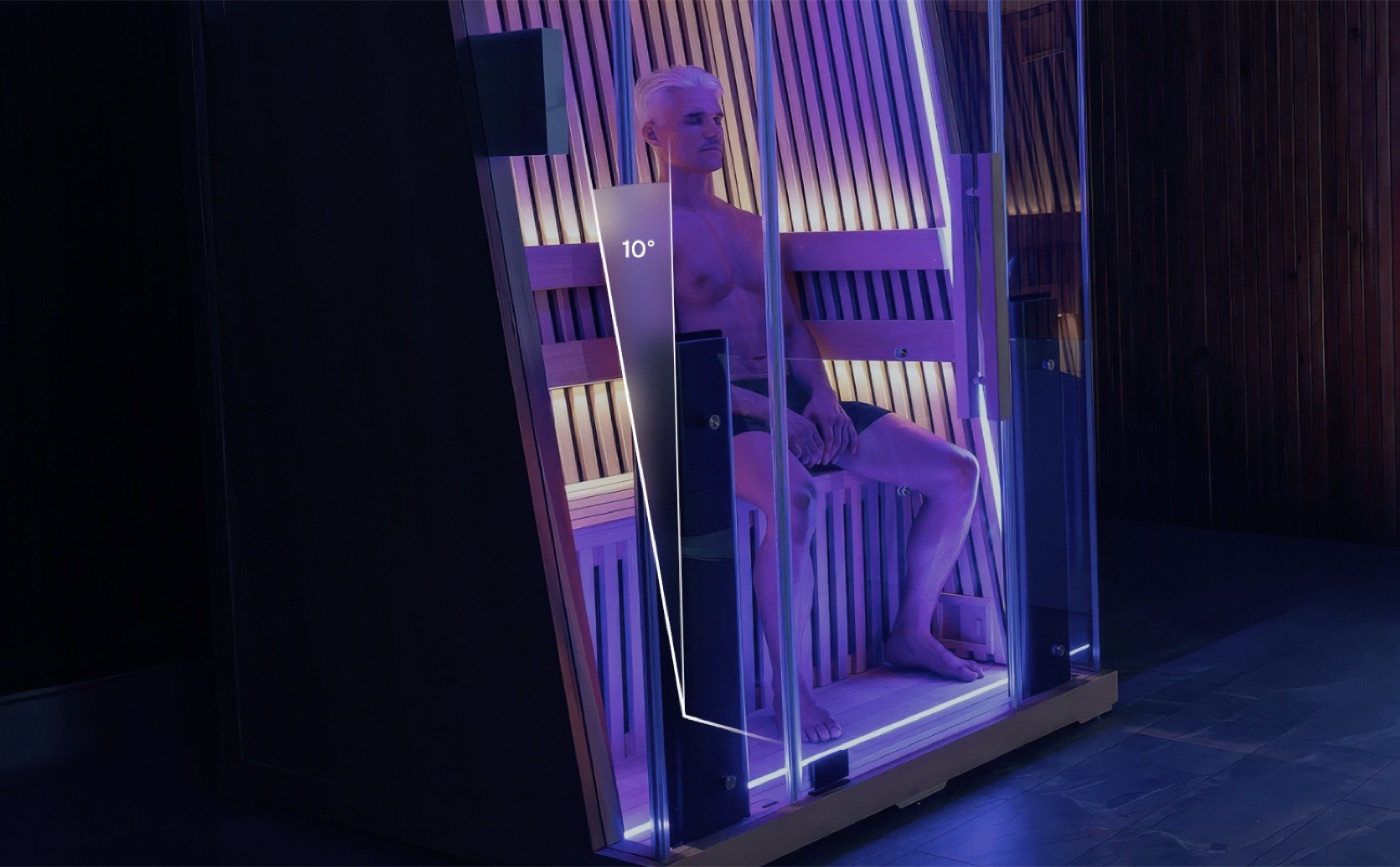Man seated in a glass-fronted infrared sauna with purple lighting, a 10 degree angle marked on the backrest